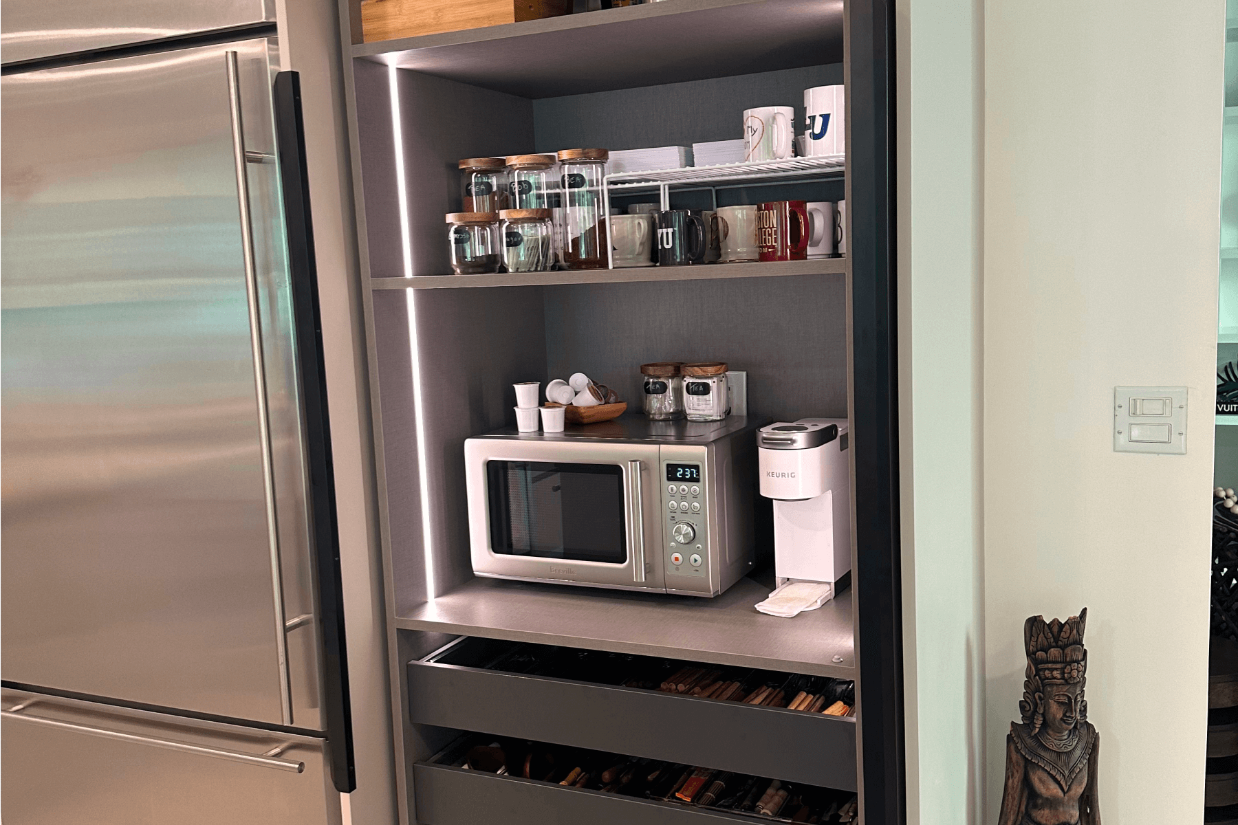 Coffee station with built-in microwave, Keurig coffee maker, and glass jars for storage inside a kitchen cabinet