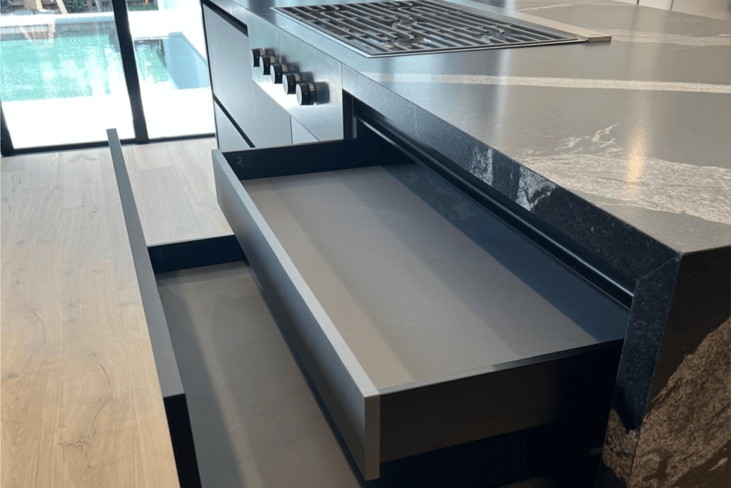 Modern kitchen drawer system under black marble countertop with built-in gas stove